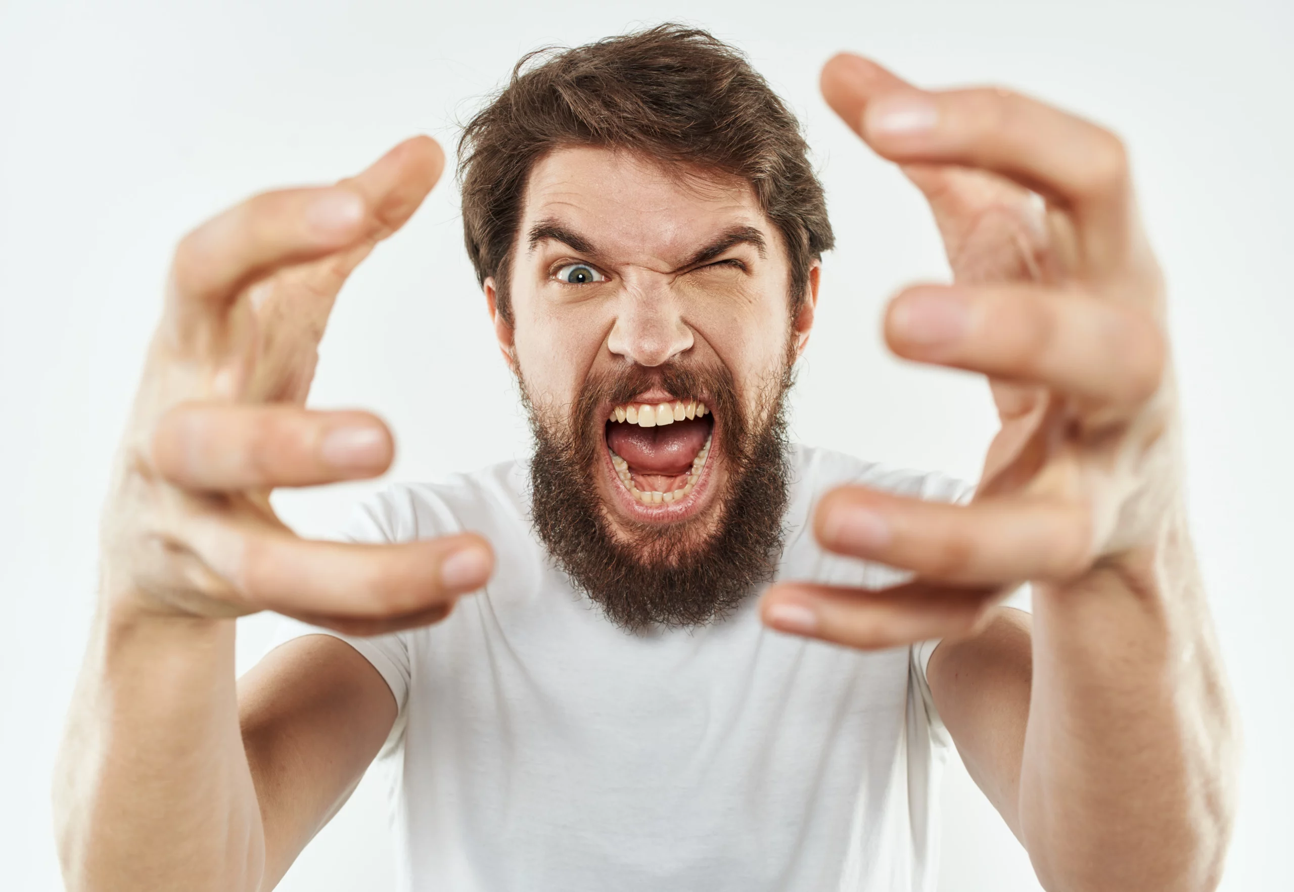 Bearded man in a white shirt screams with an intense, angry expression; wide eyes and forward-reaching hands capture aggression.