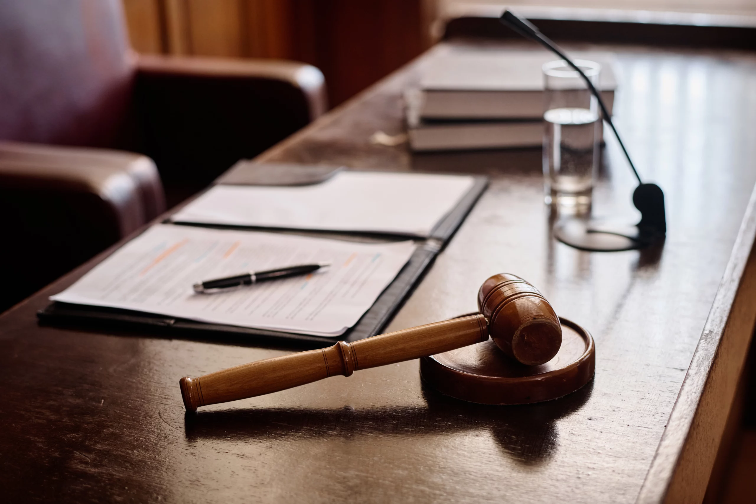 Gavel on a wooden courtroom table with a microphone, glass of water and documents — conveying the formal judicial setting in the context of Indiana’s ‘other sexual conduct’ criminal law.