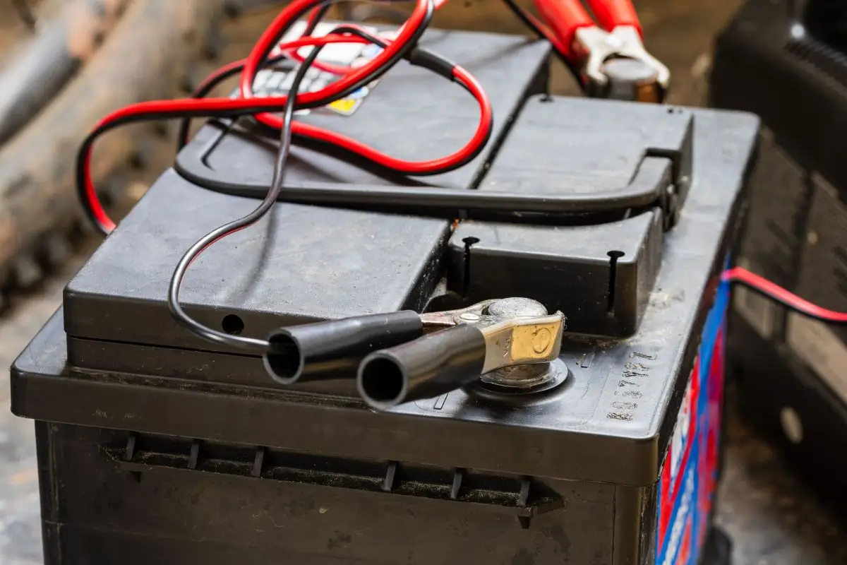Close-up of a car battery with jumper cables attached, showing a battery being charged.