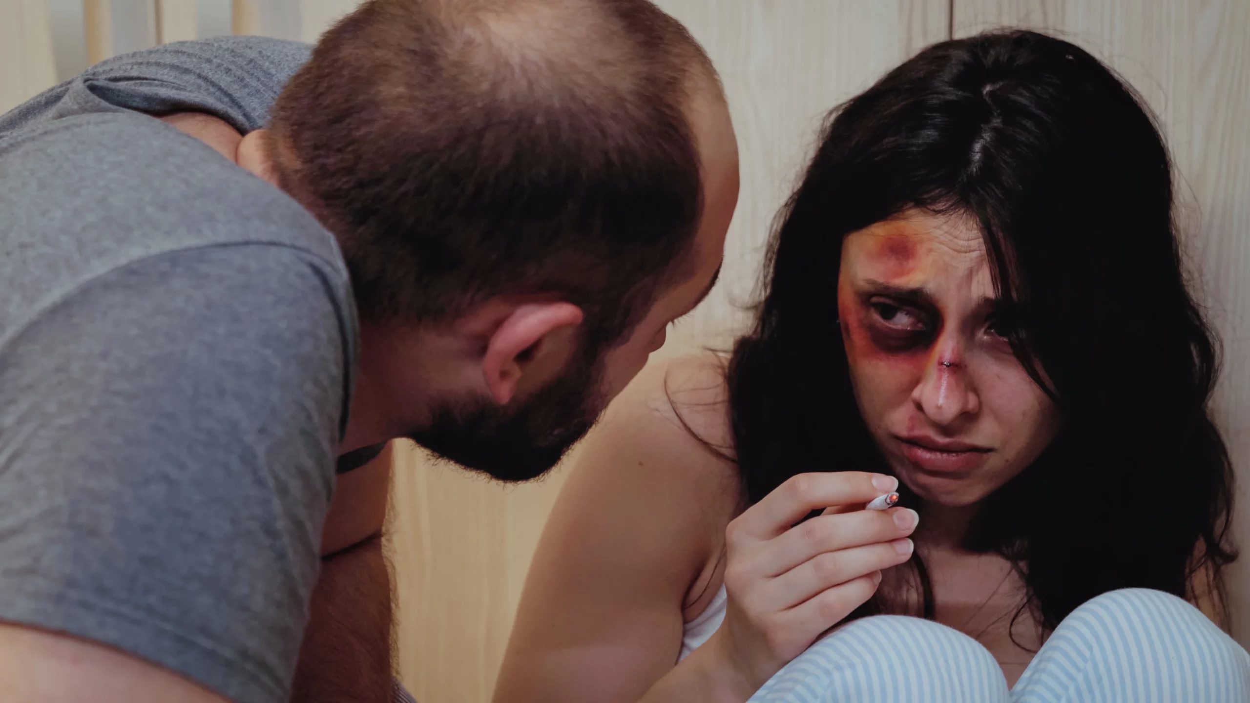 Distressed woman with bruises and black eye on floor while man appears concerned, illustrating serious bodily injury battery legal issues and defense.
