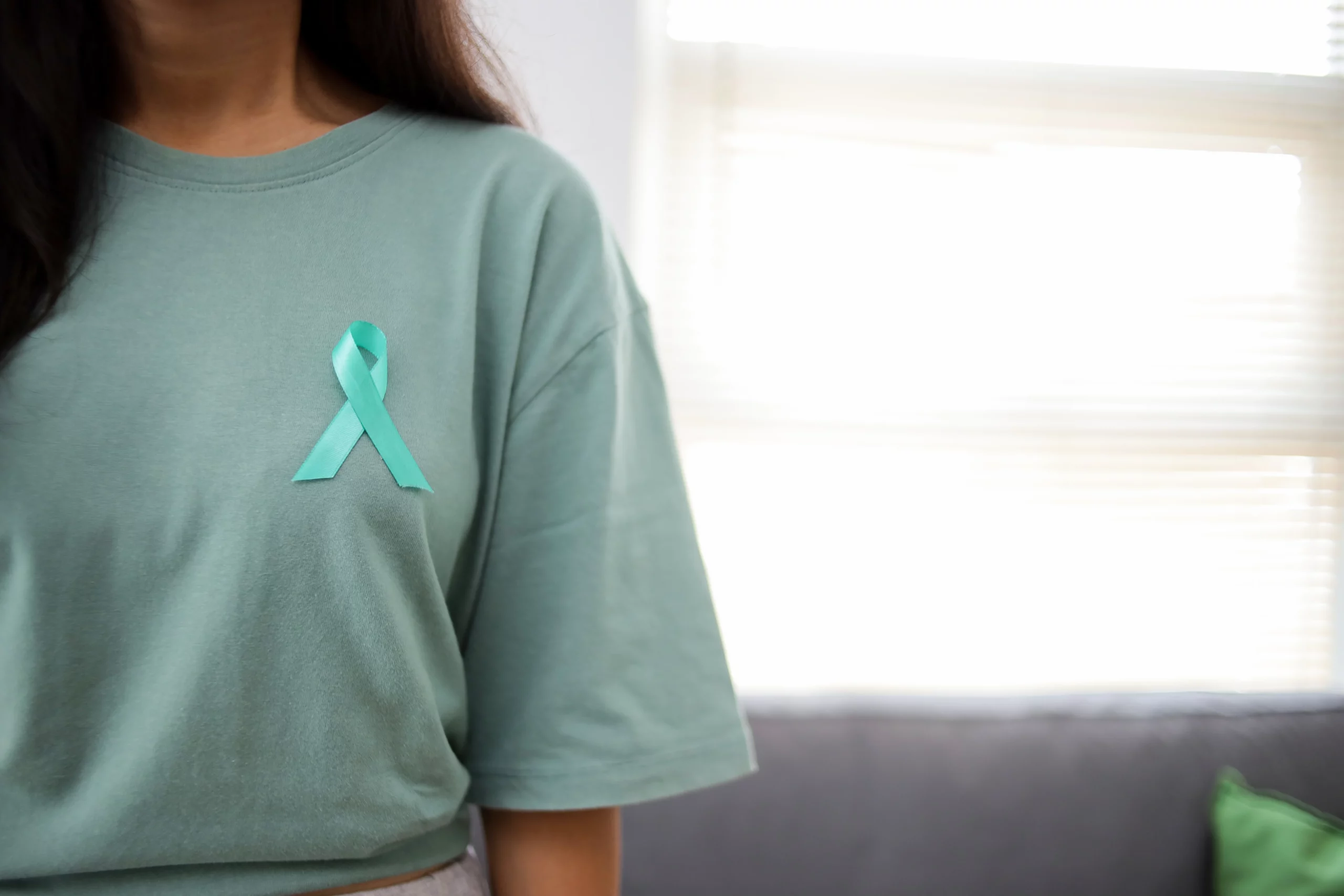 Person in teal shirt with matching ribbon pinned standing in softly lit room, illustrating awareness and rights related to Indiana mental health holds and legal protections during mental health crisis interventions.
