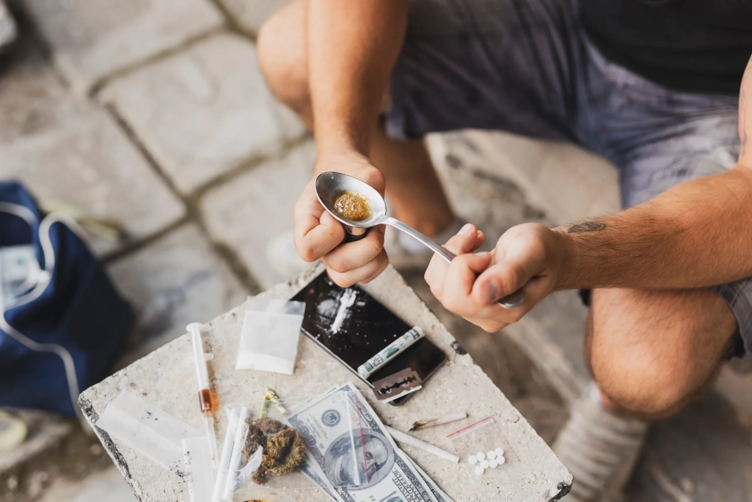 Person preparing drugs with syringes, cash, and pills representing drug possession, paraphernalia, and criminal charges for being around illegal substances