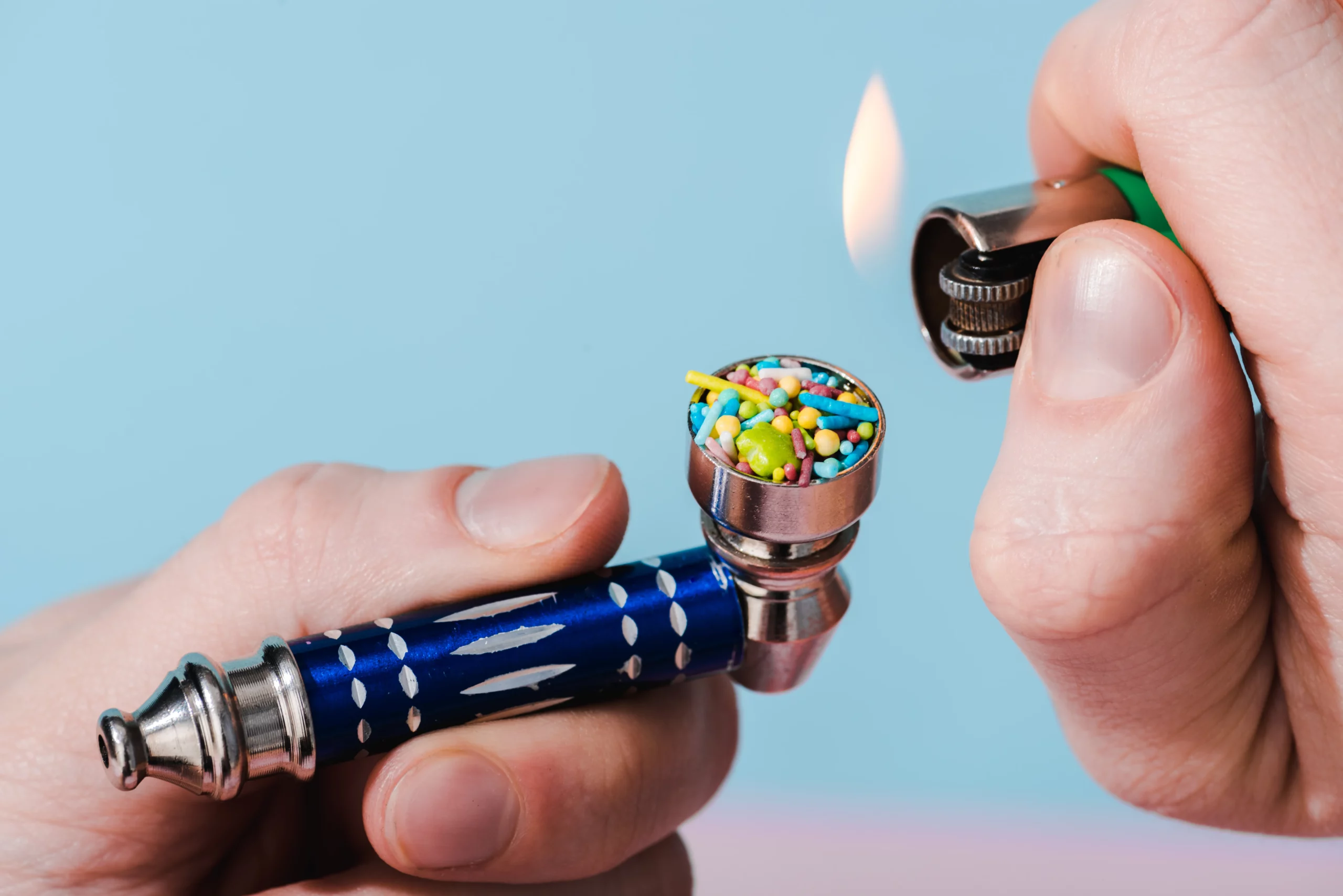 Close-up of a hand holding a pipe while another hand lights it with a lighter, illustrating items that may be considered drug paraphernalia under Indiana law.