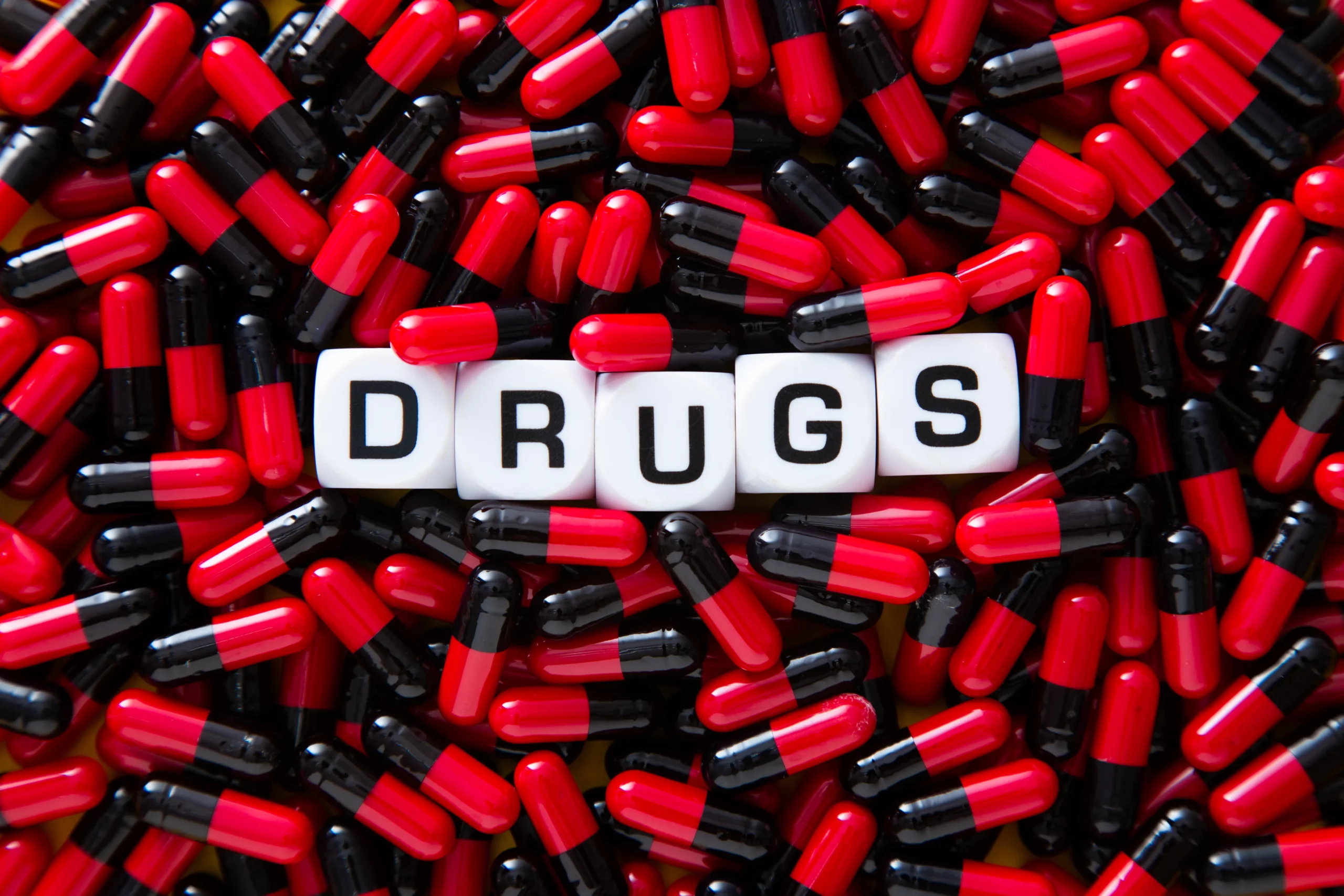 Capsules and pills spelling ‘DRUGS,’ representing designer drugs and controlled substance analogs—synthetic substances made to mimic illegal drugs but still subject to serious criminal charges and legal penalties.